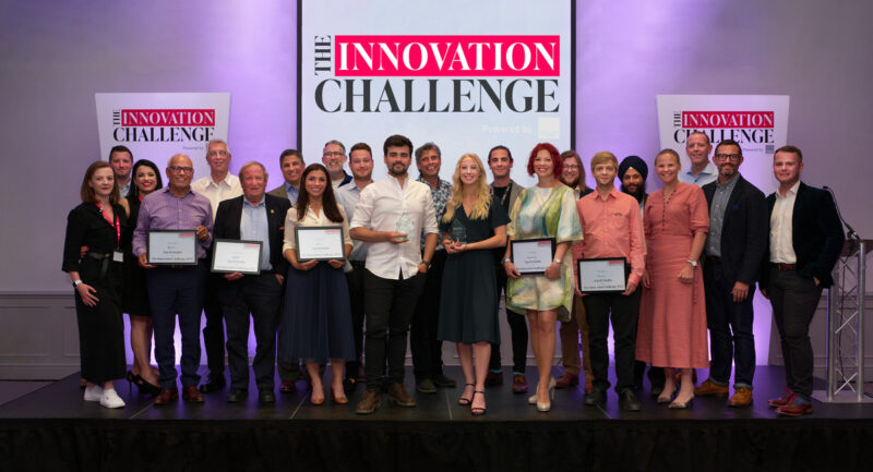 The finalists and partners of the TBAT Innovation Challenge are standing together on a stage, smiling. The finalists and winners are holding their awards.